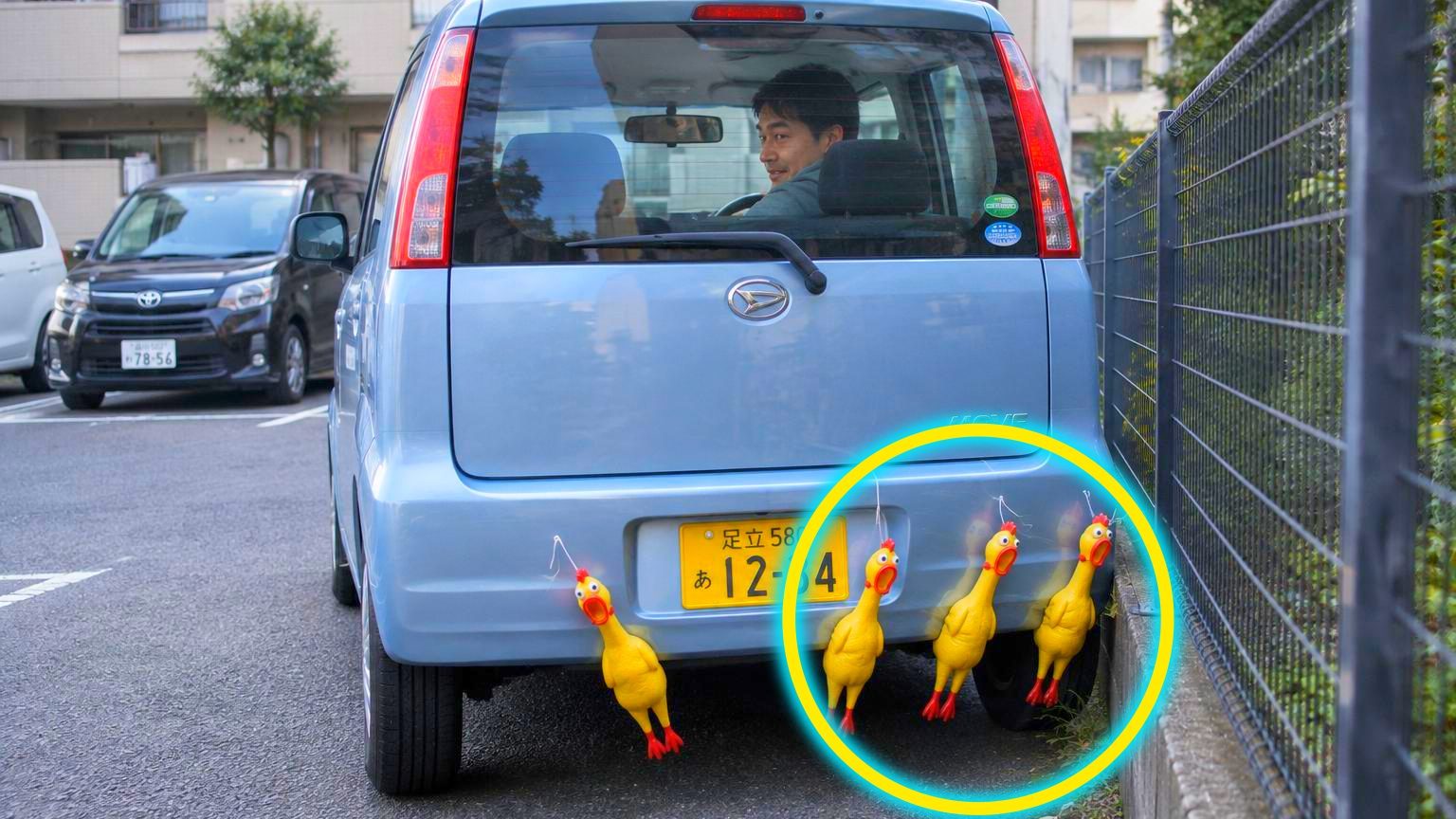 Quatre poulets en caoutchouc jaune criards suspendus par de la ficelle au grillage métallique d'une clôture de parking résidentiel, alignés à hauteur de pare-chocs