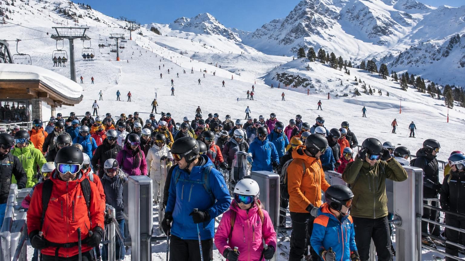 Skieurs et snowboardeurs sur une piste enneigée des Alpes françaises par beau temps ensoleillé avec remontées mécaniques en arrière-plan