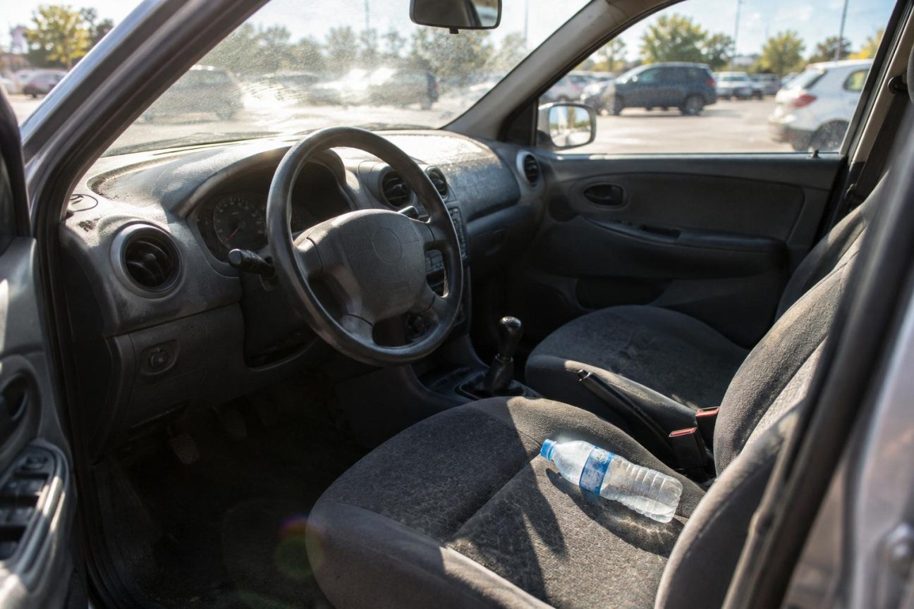 Gros plan sur une bouteille d'eau en plastique transparent posée sur un siège de voiture, avec un habitacle illuminé par la lumière du soleil d'été et le tableau de bord flou en arrière-plan
