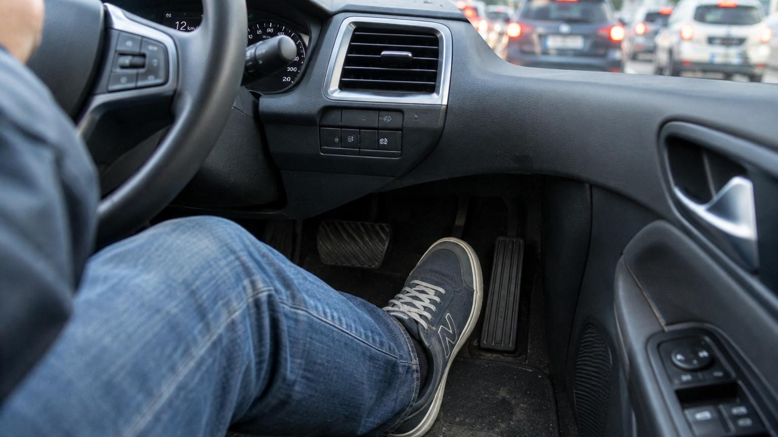 Main sur un volant de voiture électrique avec la pédale d'accélérateur visible, illustrant la technique de conduite à une pédale pour la récupération d'énergie.