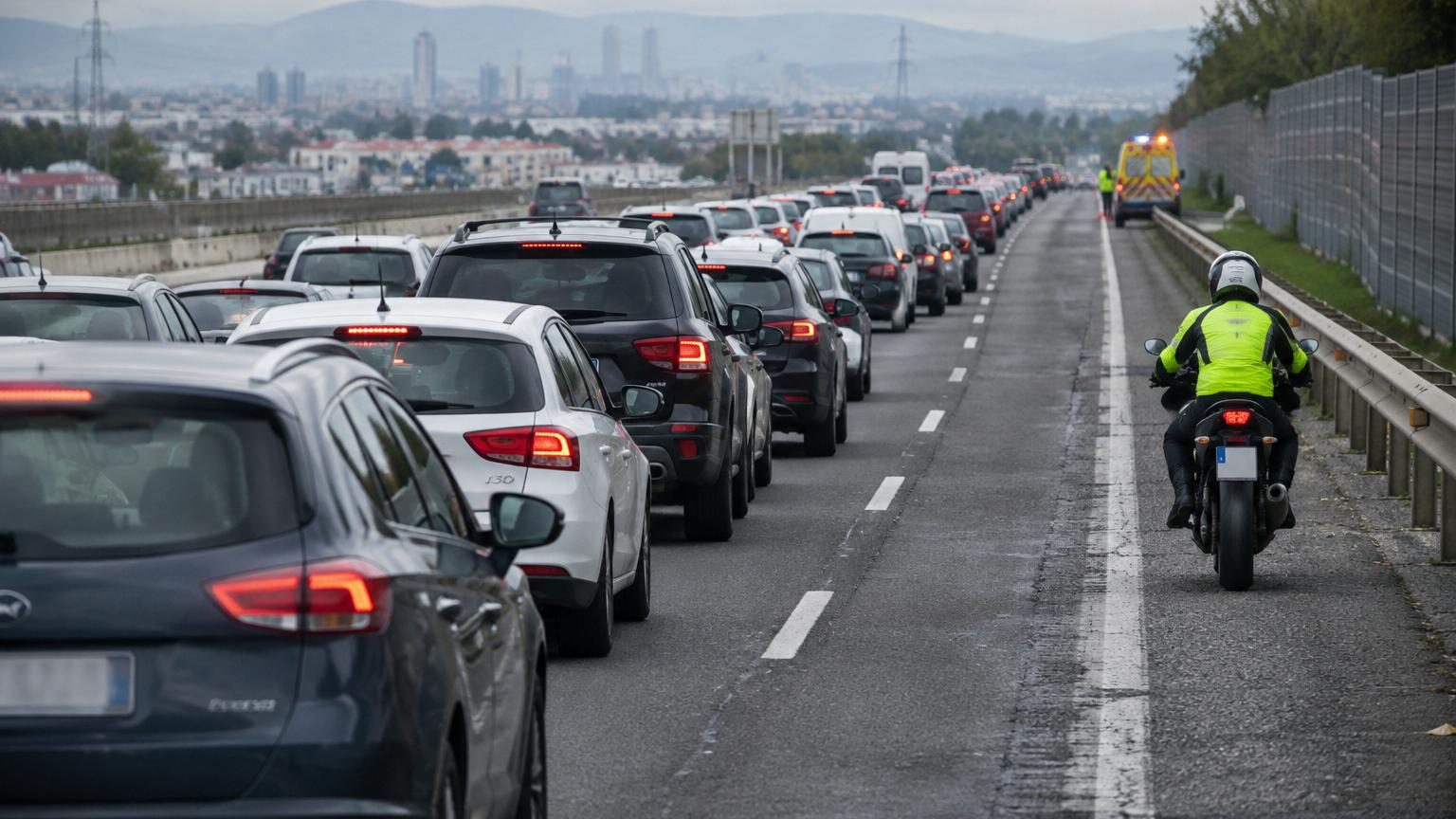 Route espagnole embouteillée avec files de voitures stationnaires et bande d'arrêt d'urgence latérale vide, panneau de signalisation visible indiquant les conditions de circulation.