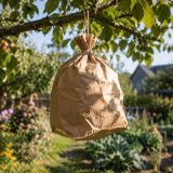 Un sac en papier kraft gonflé suspendu à une branche d'arbre, imitant la silhouette d'un nid de frelon asiatique, dans un jardin verdoyant au printemps.